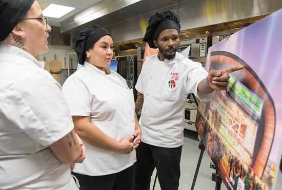 Baking and pastry arts students look over renderings as they plan to make gingerbread replicas of the new Bucks arena.