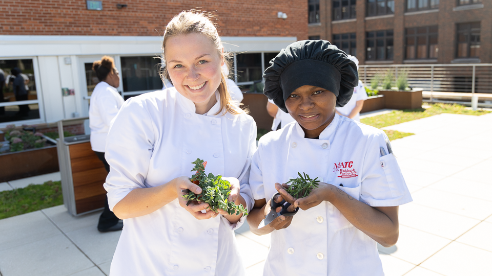 Two Students smiling and holding their freshly cut herbs 